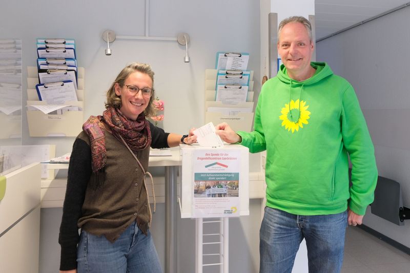 Auftakt zur aktuellen Aktion in der Blutspendezentrale Saar-Pfalz: Dominique Pegoraro (stv. Vorsitzende) und Patrick Hahl, Vorsitzender des Grünen Ortsverbands Saarbrücken-Mitte, werfen schon mal den ersten Blutspende-Scheck in die Spendenbox und sammeln für das Drogenhilfezentrum Saarbrücken.